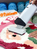 White cordless vacuum cleaner removing loose yarn from a tufted rug, practical cleaning tool for rug tufting process and yarn cleanup