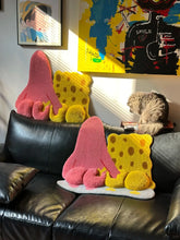 Tufted rug featuring a cute cartoon-style yellow and pink character duo shown from behind, displayed as wall decor above a sofa, highlighting the playful design and finished texture.