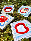 Multiple tufted apple mirror wall art pieces laid out on grass, showing various apple designs, colors, and crafted frames in a natural outdoor setting.