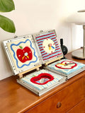 Several handmade tufted apple-shaped mirror wall art pieces displayed on a wooden dresser, showing different apple designs, bright colors, and finished fluffy textures.