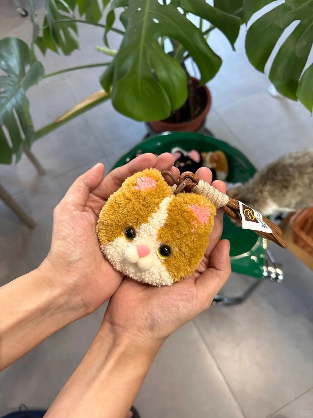 Close-up of a brown handmade tufted animal-face charm held in hand, showing soft yarn texture and small decorative details.